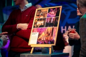 Foto van een lijst met foto's van een eerder evenement. Mensen staan er omheen